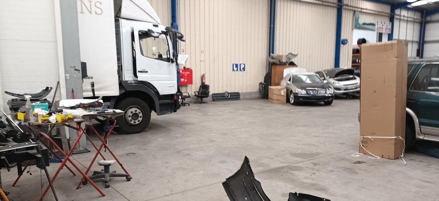 Interior amplo da oficina Auto Este com carros e um camião em reparação